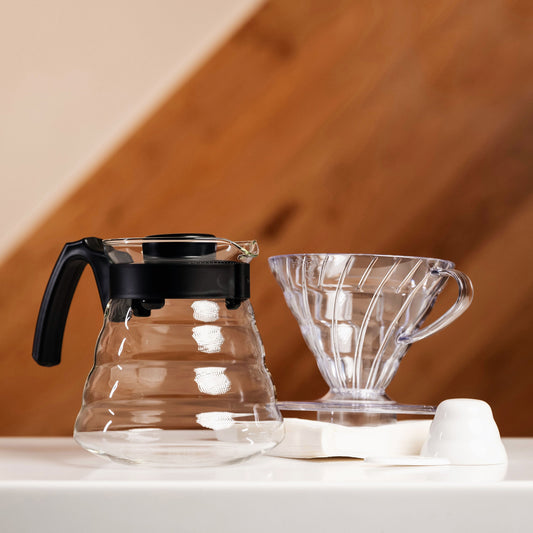 glass hario server, plastic v60 and filter papers set against a wooden background