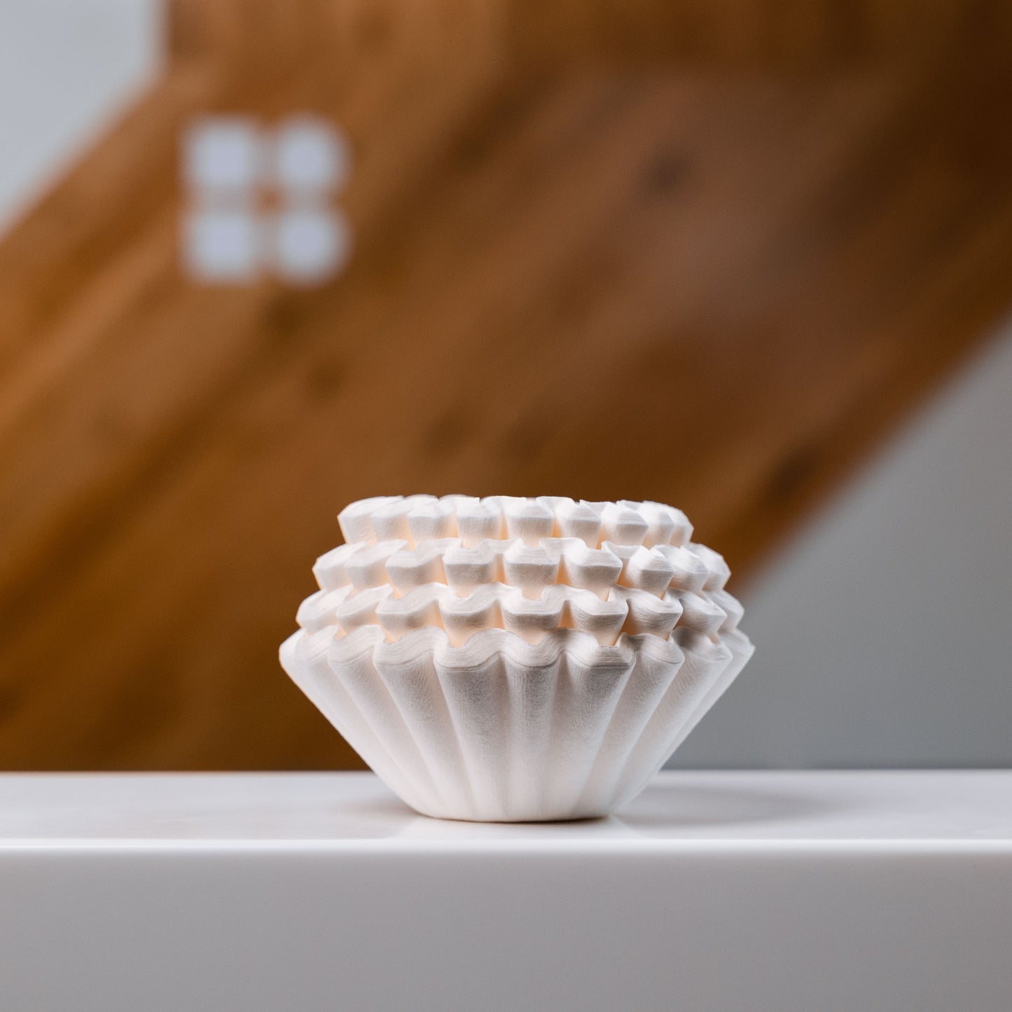 Kalita wave filter apers stacked on a white surface against a wooden backdrop