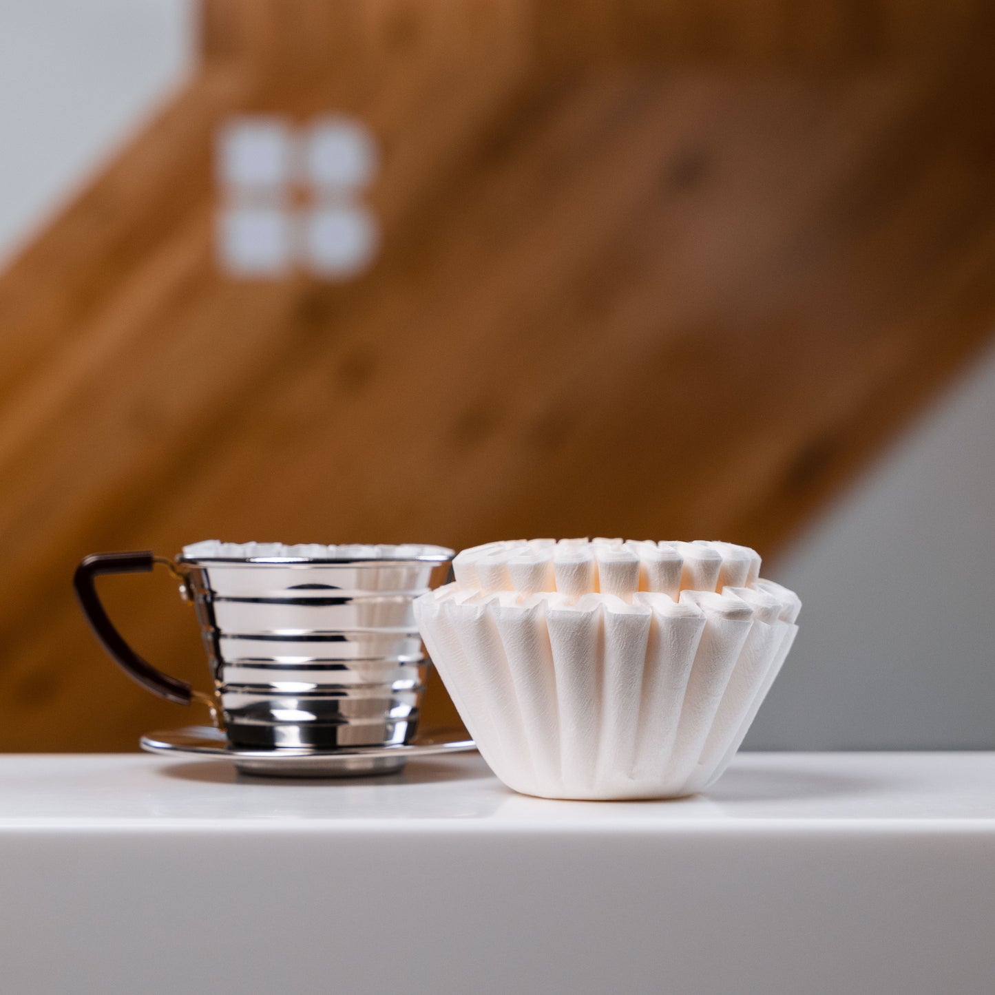 Kalita filter papers stacked on a white surface, beside a metal kalita pour over