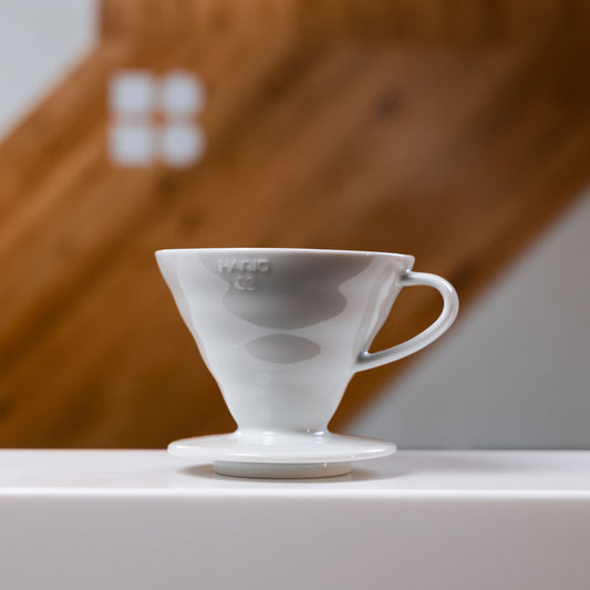 Hario V60 Ceramic Dripper in white placed against and white and wooden blurred backdrop 