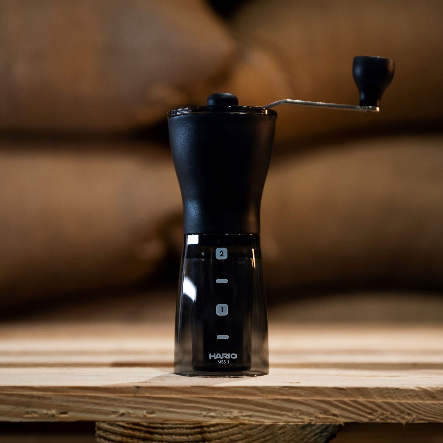 hario coffee grinder in black set against greeb bean coffee bags 